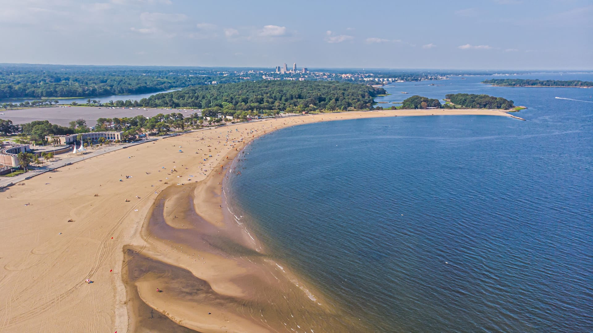 Aerial view of Orchard Beach curving along the blue water of Pelham Bay near the Chimney Sweeps Islands, with Long Island Sound beyond