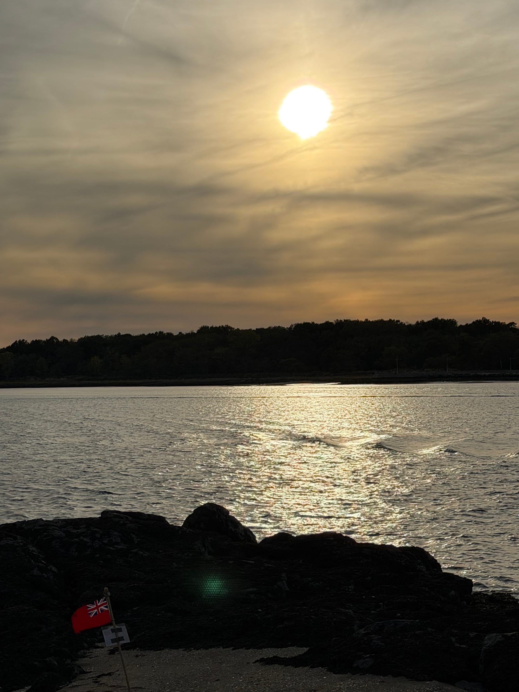 Silhouetted rocks with the small Davis Islands Red Ensign in the foreground and the sun low over the water